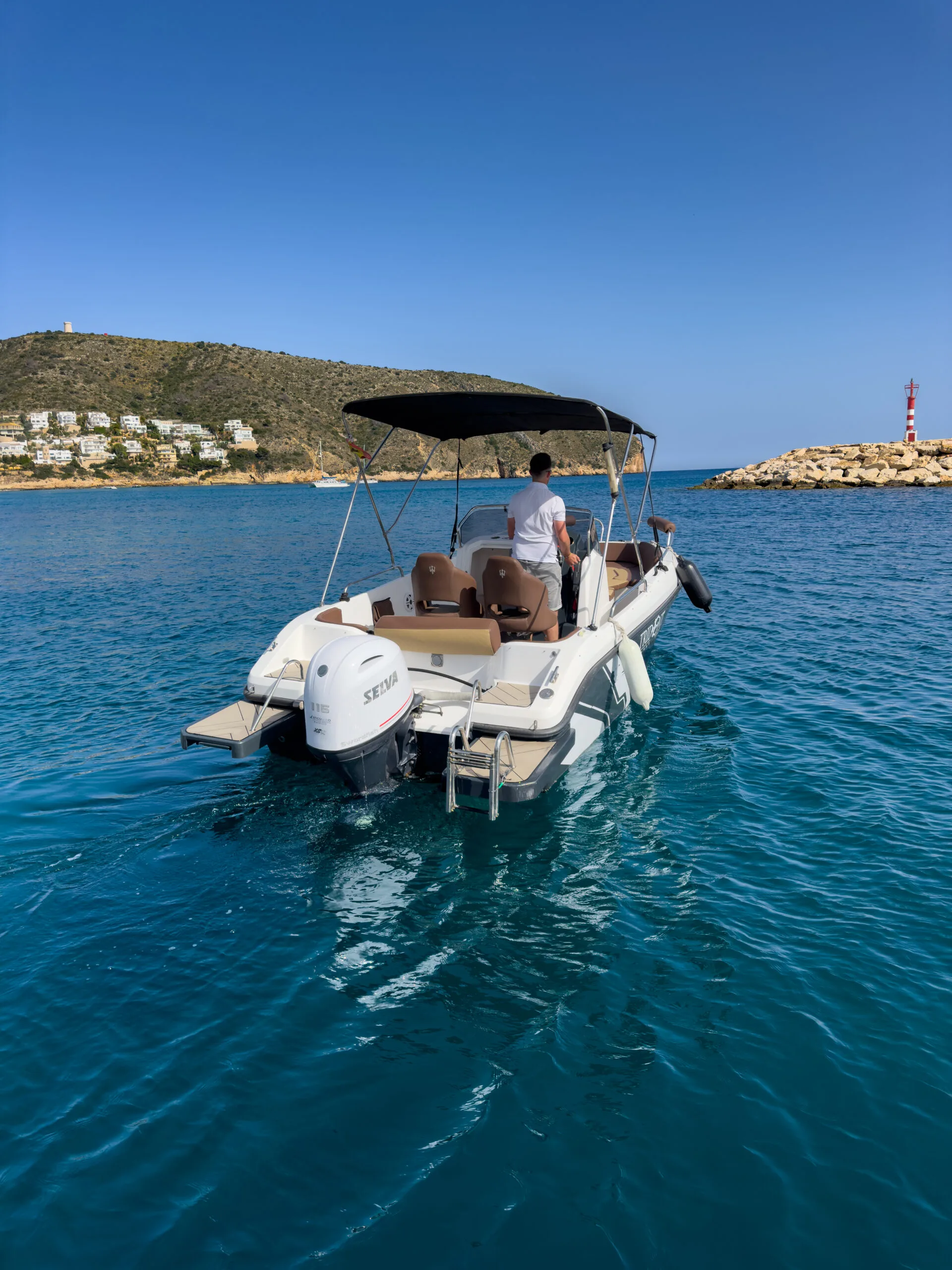 Embarcación a motor saliendo de puerto, con el patrón al timón y el faro del espigón al fondo